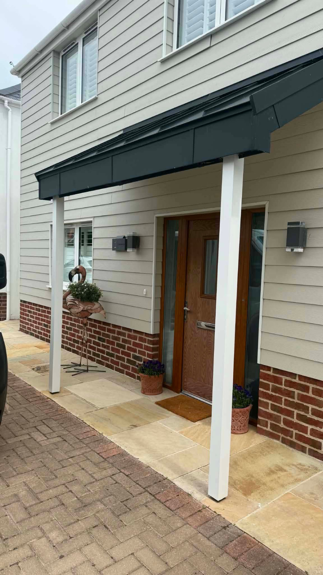 Front door canopy with two replacement white posts, timber door and brick plinth